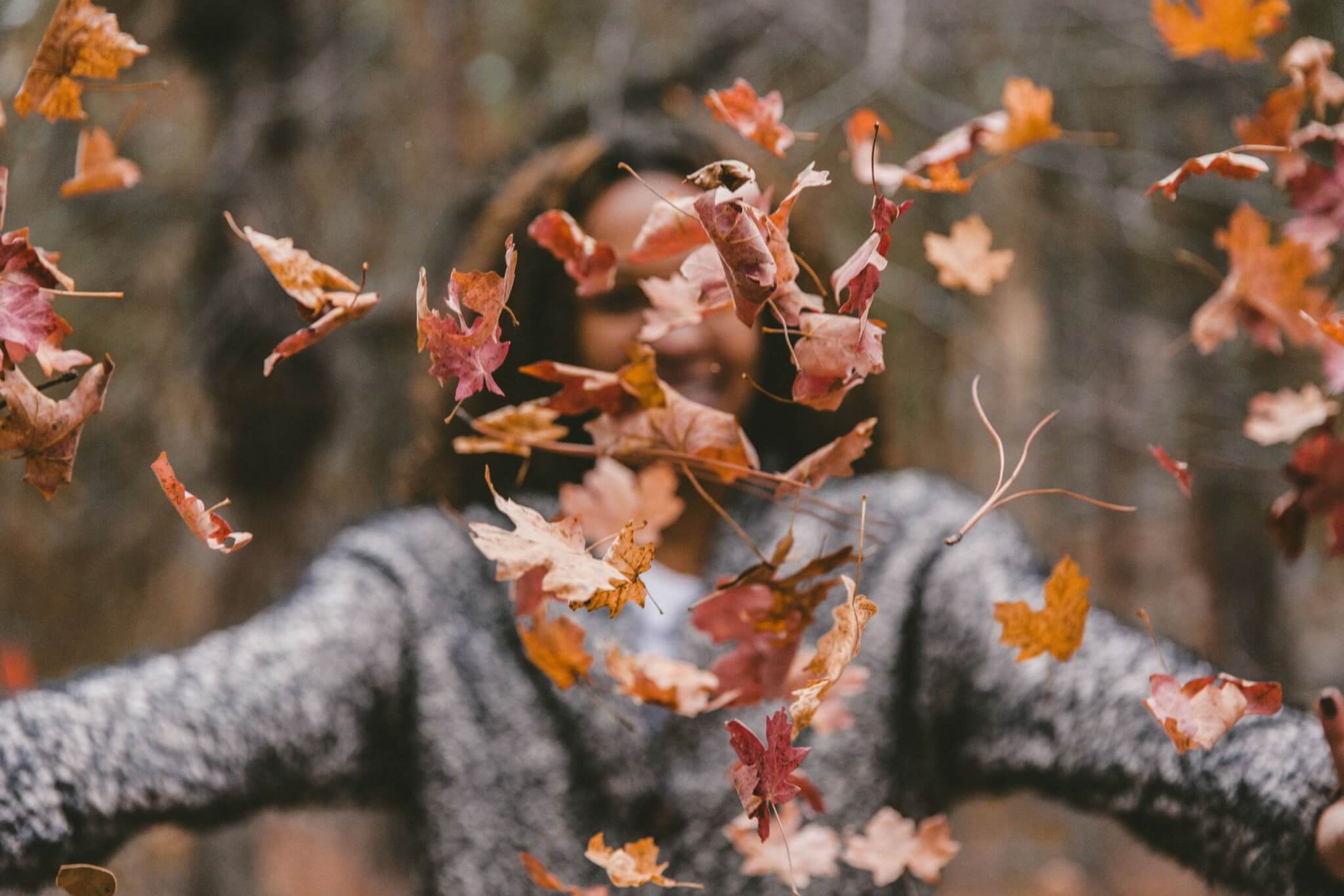 vrouw in bos gooit met herfstbladeren